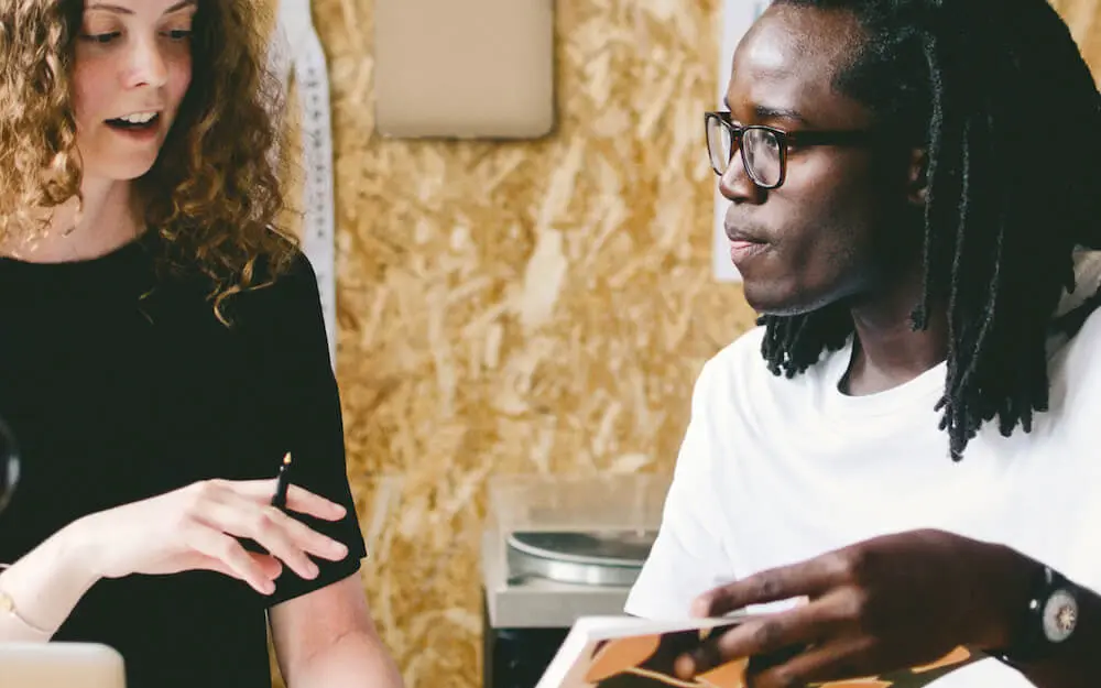 Due persone discutono mentre guardano un documento, in un ambiente lavorativo informale.