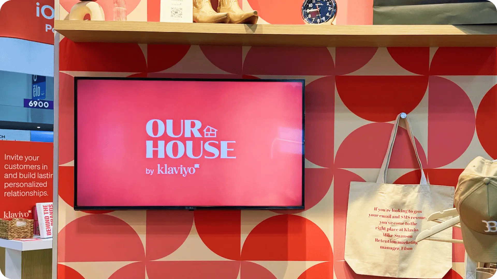 Display with "OUR HOUSE by klaviyo" on a screen, surrounded by promotional materials and a tote bag with text.