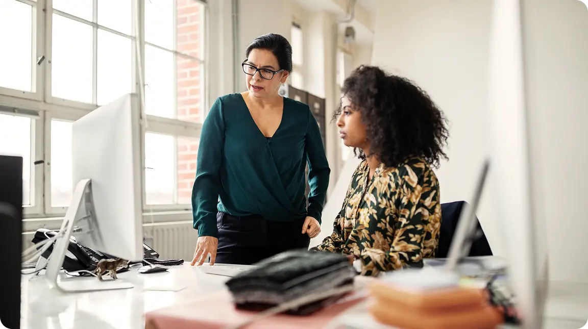 Two coworkers discussing reviews at a desk in an open loft office space
