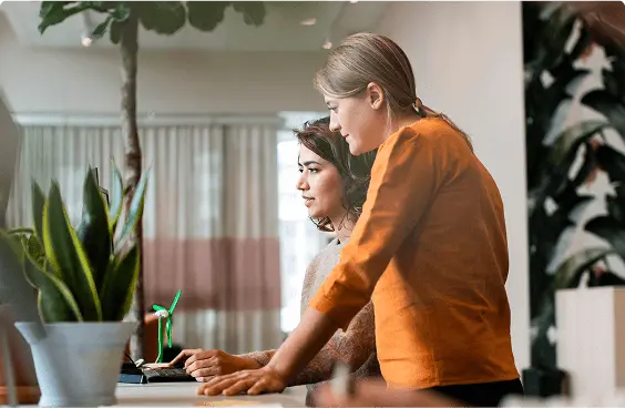 Photograph of 2 colleagues talking at a workspace.