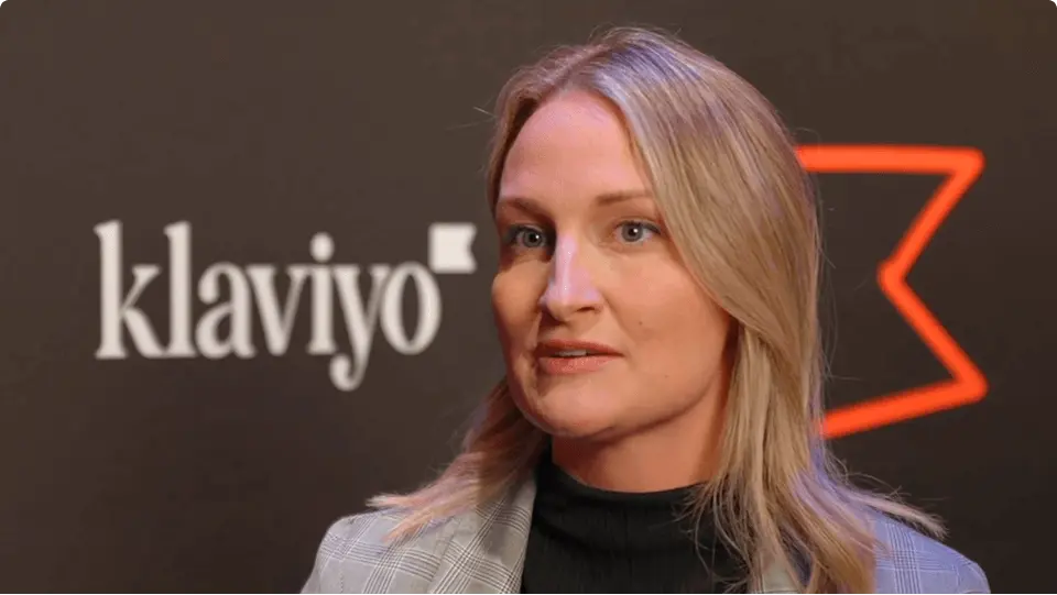 A woman with blonde hair speaks in front of a Klaviyo logo.